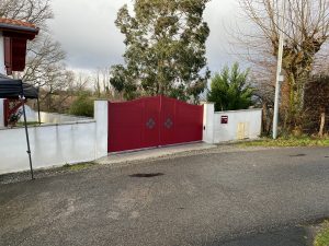 Portail battant fabrication en pente bas en biais chapeau de gendarme lames pleines et décor personnalisé croix basque en triple tôle en aluminium soudé BREDOK motorisation FAAC installé par AED64 au coeur du Pays Basque